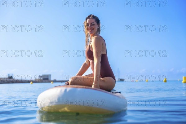 Smiling woman sitting on a paddleboard in clear blue waters, enjoying a sunny summer day. Perfect scene for leisure and outdoor water activities