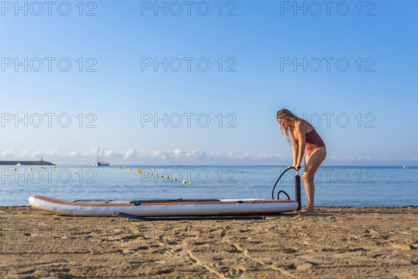Woman inflating her paddle board on a beautiful sandy beach, preparing for a summer adventure on the calm sea