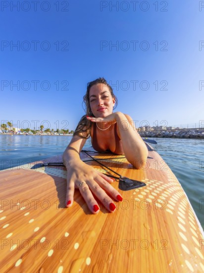 Young woman lying on a paddle board, soaking up the sun and enjoying the warm summer day while surrounded by the tranquil sea