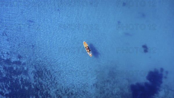 Aerial view of a sportswoman paddle surfing on a sup board in the transparent waters of the ocean during summer vacation