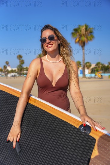 Smiling woman carrying her paddle board along a sunny beach, embracing the excitement of a summer adventure by the ocean