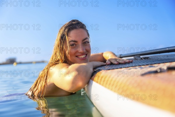 Cheerful woman relaxing on a paddleboard in clear blue water, embracing the joy of summer and outdoor adventure