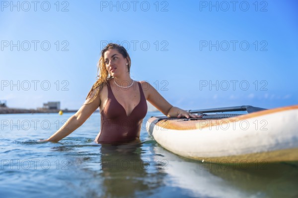 Young woman wearing swimsuit relaxing in the sea next to her paddle board on a sunny summer day