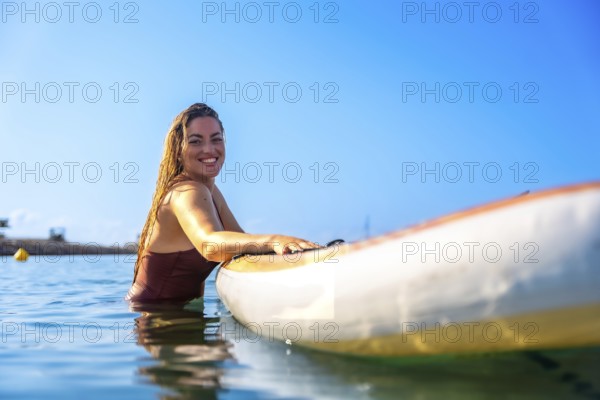 Woman enjoying paddle surfing in clear blue water, showcasing a joyful summer experience under a sunny sky