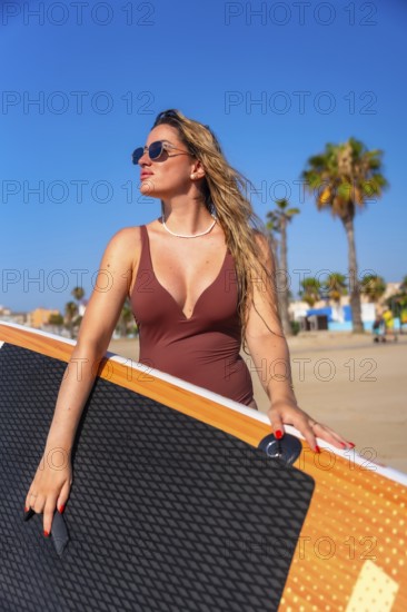 Surfer holding her paddle board on a sunny summer day at the beach, soaking up the sun and feeling the ocean breeze, ready for adventure