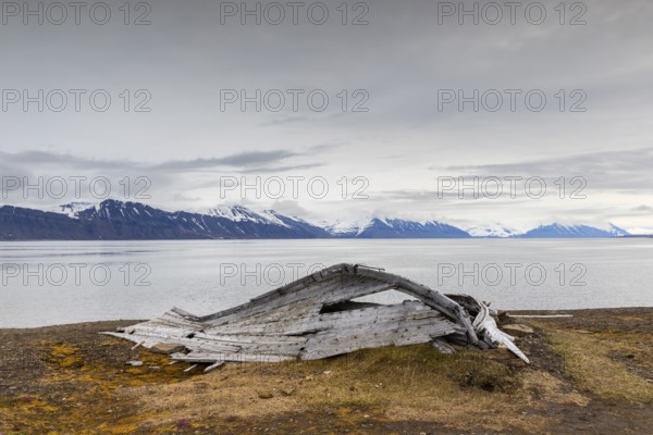 Broken wooden boat in front of mountain range, snow, sea, Bamsebu, Spitsbergen, Svalbard