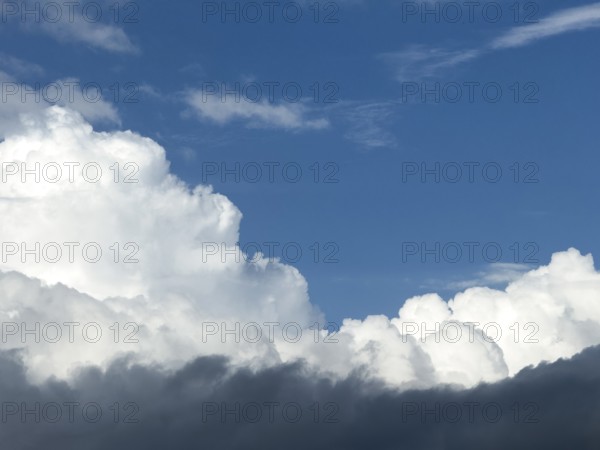 At the bottom of the picture grey nimbostratus clouds, above white cumulus cumulus clouds in front of a blue sky, International