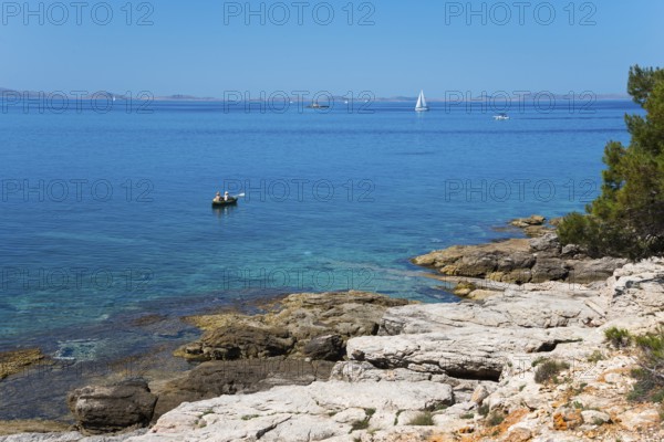 Rocky coast with clear water and sailing boat under blue sky, Slanica, town of Murter, island of Murter, Dalmatia, Croatia
