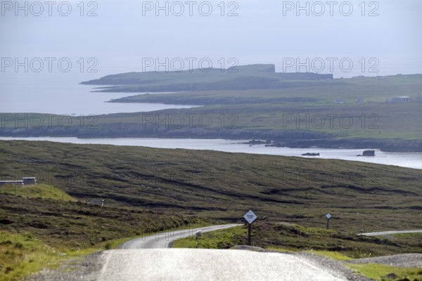 Coastal road winds through rolling countryside with views of the sea and distant islands, Eshaness, Mainland, Shetland Islands, Scotland, United Kingdom