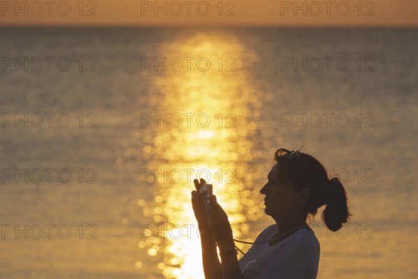 Woman, 40-50 years old, taking a photo with her smartphone at sunset, Koh Mook Island, Andaman Sea, Thailand, Southeast Asia