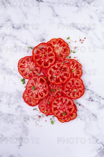 Freshly sliced ripe tomatoes arranged on a marble surface with microgreens and sea salt for a culinary presentation