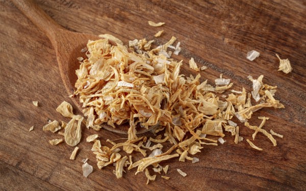 Smoked onion flakes, on a wooden spoon, wooden table, close-up