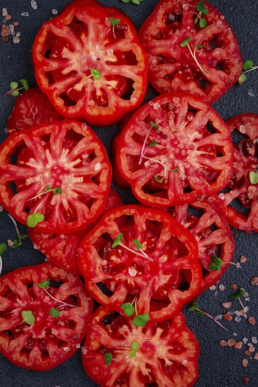 Freshly sliced ripe tomatoes arranged on a textured dark surface with herbs and salt scattered around