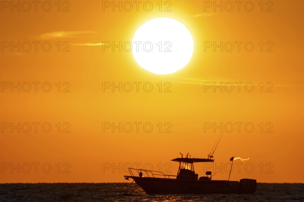 The sun rises behind a boat on the Costa Rei, a coastal section of the Italian Mediterranean island of Sardinia, Monte Nai, Costa Rei, Sardinia, Italy. Sardinia