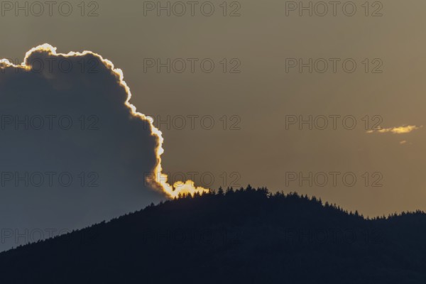 A radiant sunset conjures up warm colours as the clouds hang over a mountain range. Trees line the slopes and adorn the breathtaking sunset. The sky transitions to night. Bas rhin, Alsace, Grand Est, France