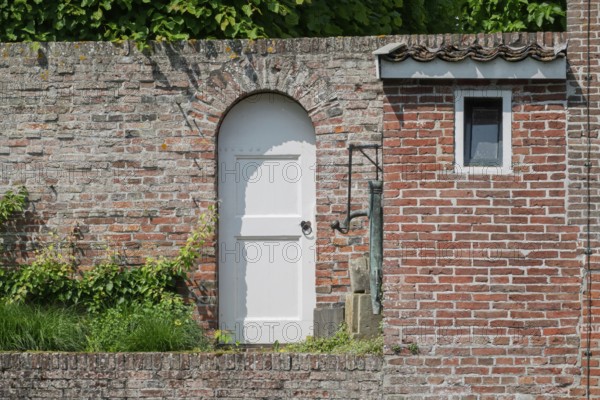 White arched door in an old brick wall with green ivy above, Borg Verhildersum, Leens, province of Groningen, Netherlands
