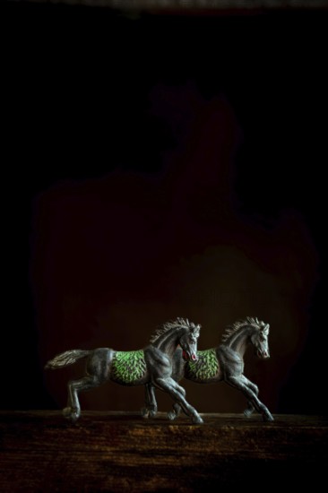 Two intricately designed horse figurines are positioned side by side, appearing to run forward. The dark background highlights their detailed feature