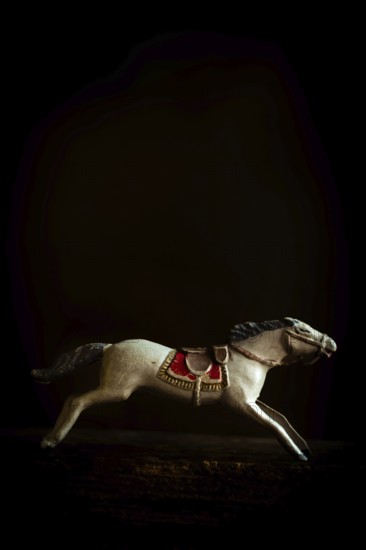 A vintage toy horse captures a galloping stance, emphasizing the intricate craftsmanship of its saddle and mane. The dark background enhances the nostalgia and charm of the piece