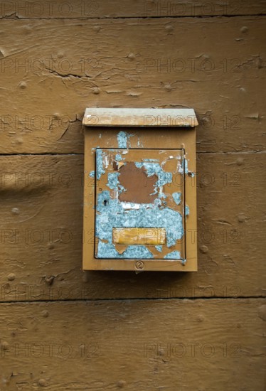 A weathered mailbox hangs on a rustic wooden wall, showcasing chipped paint in blue and brown tones. This scene suggests stories of past correspondence in a quiet neighborhood. France