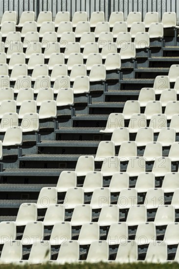 Empty white seats neatly arranged in rows await spectators at a stadium. The absence of an audience highlights the setting and the architectural design of the venue