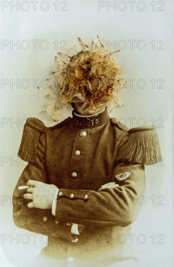 A soldier stands confidently, sporting a distinctive uniform with epaulettes, while a curious arrangement of flowers covers his head. The sepia tones highlight the unusual composition and moment