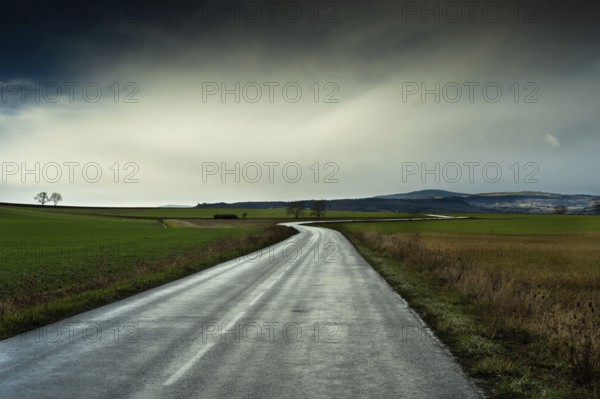 A winding road stretches through green fields under a cloudy sky, showcasing the beauty of the landscape with distant mountains in view. Auvergne. France
