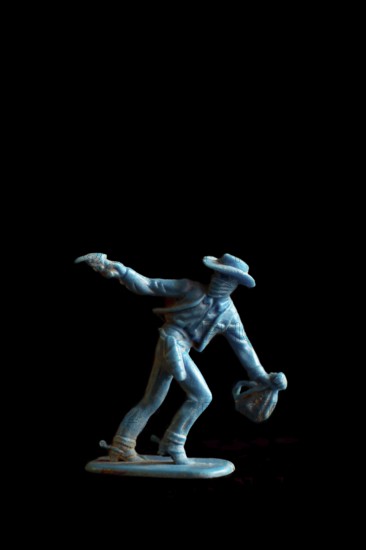 A vibrant blue cowboy action figure strikes a dramatic pose while drawing a weapon, set against a dark background that enhances the sense of adventure