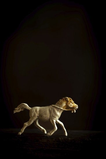 A finely crafted brown wooden horse figure is captured in motion, depicting a galloping stance as it trots on a dark surface, showcasing intricate details against a minimalist backdrop