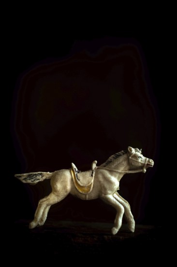 A detailed toy horse is captured in motion, showcasing its intricate design and craftsmanship. The dark background enhances the horse's striking features and vintage charm