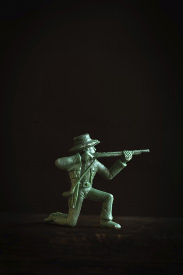 A detailed figurine of a gunslinger kneels and aims a rifle in a low light setting. Striking shadows enhance the figure's features, creating a tense and action-filled atmosphere