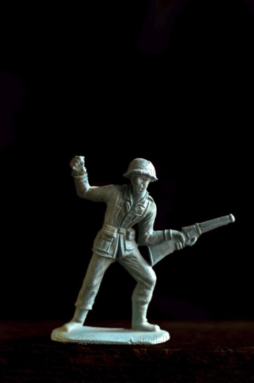 A plastic soldier figurine stands confidently with a rifle and raised fist, captured in warm lighting on a dark background