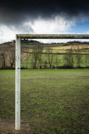 An old and weathered football goalpost stands empty on a green field, surrounded by a peaceful rural landscape. Auvergne. France