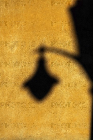 Soft afternoon light creates a striking shadow of a lantern on a textured yellow wall. The warm colors add depth, enhancing the tranquil atmosphere of the setting