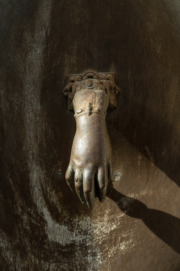 A decorative hand-shaped door knocker is firmly mounted on a weathered wooden door showcasing rich textures and an antique charm in a historic building