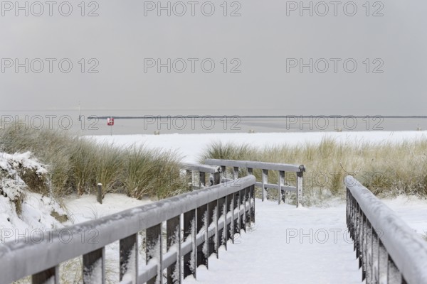 Winter day, onset of winter, wooden plank path leads through the snow-covered dune landscape to the North Sea, Norddeich, Lower Saxony, Germany