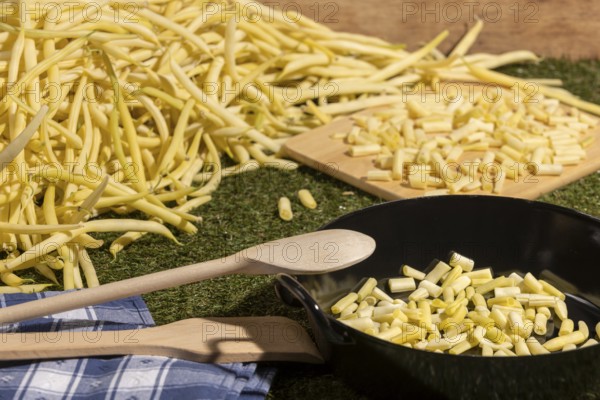 Pan with sliced yellow runner beans and a wooden spoon, beans in the background