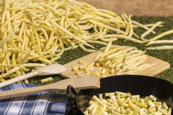 Yellow runner beans next to a cooking pot with sliced beans and wooden spoons