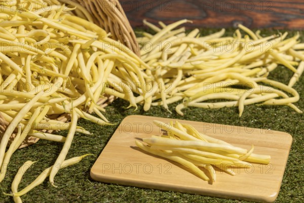 Basket with yellow beans on green grass, some beans on a board