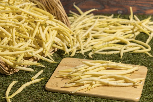 A basket of yellow beans, some on a board on a green background