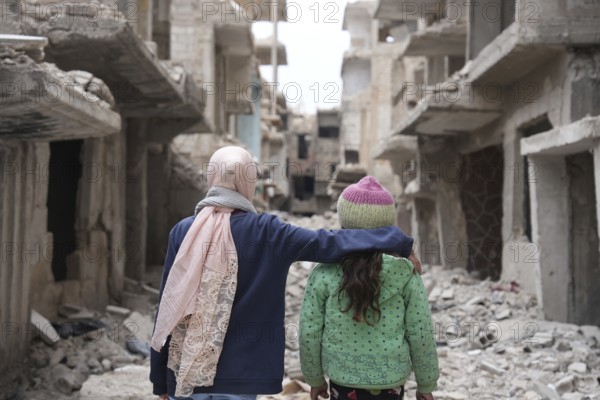 Two girls stand in shock in front of a building destroyed by the war in Syria
