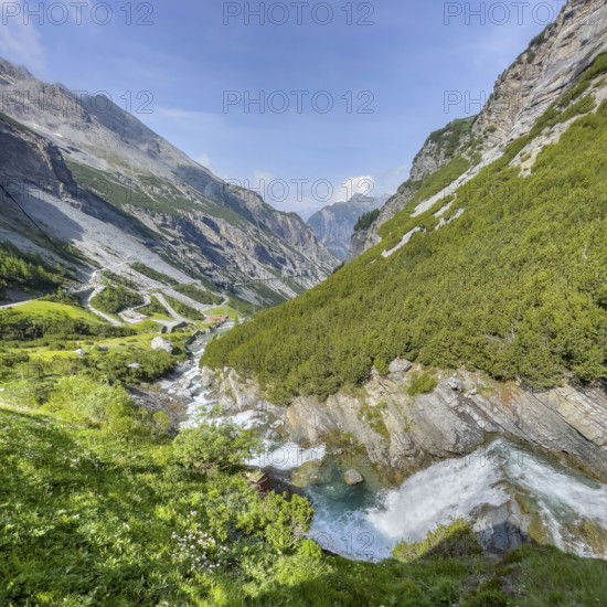 View of the Cascata dello del Braulio waterfall on the right foreground, in the background southern ascent to the descent from the Alpine pass Stelvio Pass, Valdidentro, Lombardy, Italy
