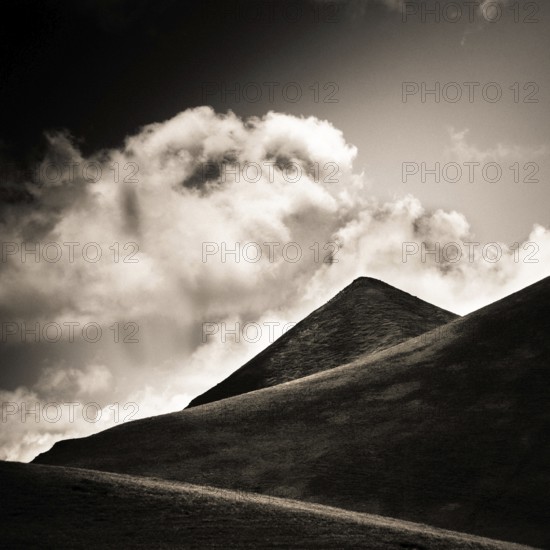 A striking view of a mountain peak stands tall against a backdrop of swirling clouds. Sancy Massif, Puy de Dome, Auvergne Rhone Alpes, France