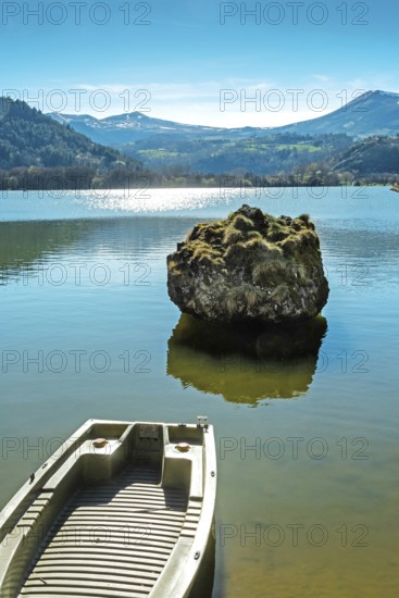 Lake chambon reflects the stunning blue sky and surrounding mountains. A small boat rests at the shore. Puy de Dome. Auvergne. France