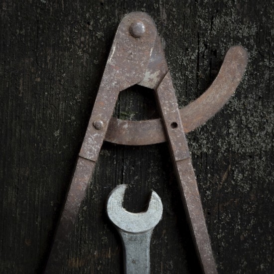Two old metal tools, a caliper and adjustable wrench, lay on a textured wooden surface, revealing their wear and the beauty of traditional craftsmanship over time