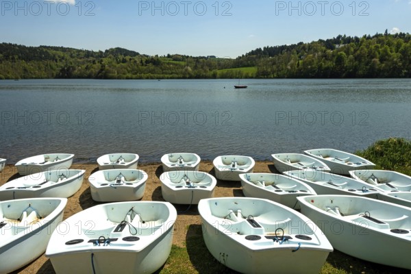 Rowboats rest neatly along the sandy shore of a tranquil lake surrounded by lush greenery. Puy de Dome. Auvergne. France
