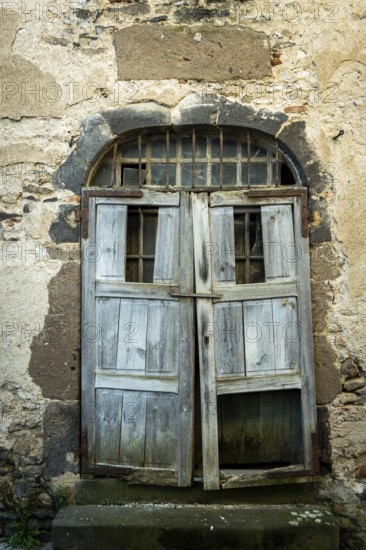 A rustic wooden door stands ajar in an aged stone wall, showing signs of weathering and decay. The historical architecture features unique textures and colors, evoking a sense of timelessness. France