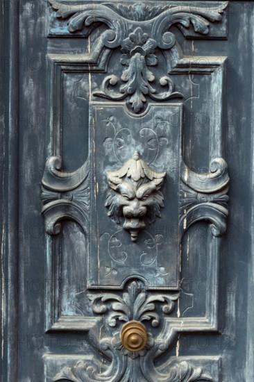 A striking door features detailed carvings and a lion head knocker, blending antique charm with wear marks that tell stories of a bygone era