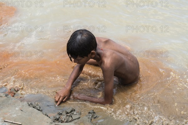 A boy sits in the bank of Brahmaputra River as he bathe to seek relief from the intense summer heat in Guwahati, India, on June 26, 2025