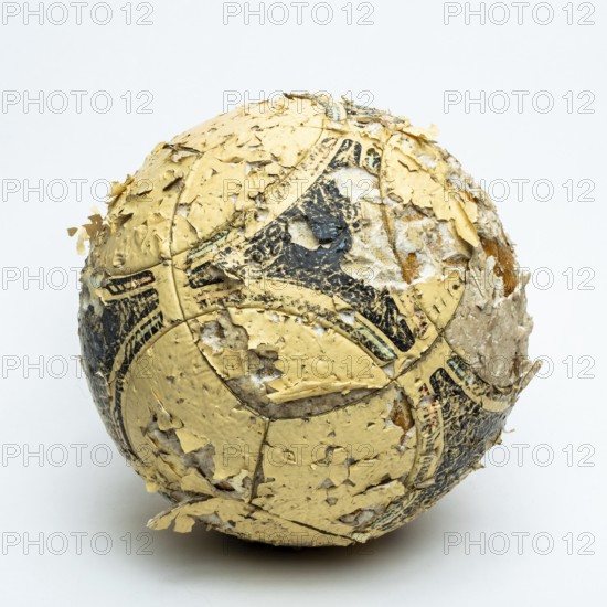 A worn football ball rests against a neutral background, displaying significant peeling and faded markings. The condition reflects years of use, capturing the essence of play and nostalgia