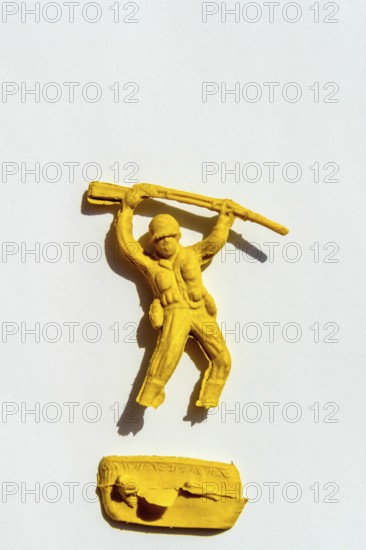A bright yellow toy soldier holds a rifle above his head, showcasing an imposing stance. The figure stands out against a simple white background